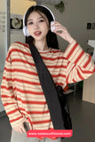 Person wearing a red and beige striped sweater with a black strap over their shoulder, indoors.