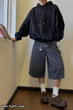Person wearing a black hoodie and dark shorts standing indoors.