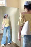 Person wearing a yellow top and blue jeans, standing in front of a mirror.
