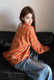 Person wearing an orange plaid shirt and blue jeans sitting on a black couch.