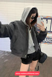 Person taking a selfie in a gray jacket and black shorts against a tiled wall.