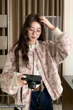 Woman holding a camera indoors, wearing a floral jacket.