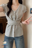 Person wearing a checkered shirt and blue jeans, posing indoors.