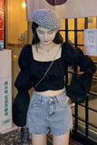 Person wearing a black top and denim shorts with a checkered hat indoors.