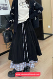 Person wearing a black outfit with a plaid skirt, holding a black handbag indoors.