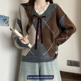 Person wearing a patterned sweater with a bow tie, holding a book, against a neutral wall.