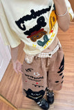 Person wearing a white shirt with cartoon designs and brown pants with black cat prints on a wooden floor.