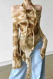 A woman wearing a brown and beige tie-dye halter top with ruffled details and light blue jeans, standing against a plain light gray wall.