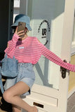 Person wearing a pink off-shoulder top and denim shorts standing in front of a door with a visible brand logo.