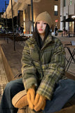 Person wearing a plaid coat and beige beanie sitting outdoors at night.