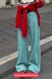Person wearing a red sweater, striped shirt, and teal pants on a street.