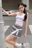 Woman in a white top and gray skirt standing on a street.
