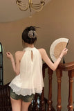 Woman in a white top and green shorts holding a wooden fan indoors.