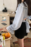 Person wearing a light blue blouse with ruffled sleeves in an indoor setting.