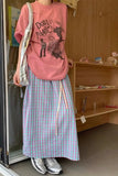 Person wearing a pink graphic t-shirt and plaid skirt standing indoors.