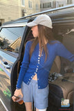 Person wearing a blue cardigan and white cap standing next to an open car door.