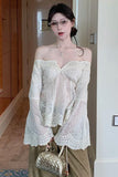 Woman wearing a white lace off-shoulder top and holding a gold handbag indoors.