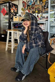 Person wearing a plaid jacket and jeans sitting in a chair in a room with a refrigerator and tools on the wall.