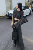Woman in a long gray sweater and skirt holding a black handbag on a street.