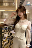 Woman in a white lace outfit standing in an elegant interior setting