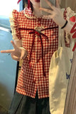 Person wearing a red and white checkered dress with a large bow, standing indoors.