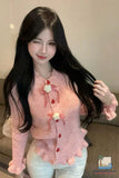 Woman wearing a pink sweater with decorative buttons and flowers, sitting on a couch.