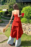 Woman in a red dress holding a red bag outdoors with greenery and stone wall in the background