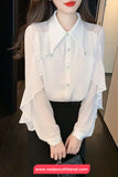 White blouse with ruffled sleeves worn by a person, with a blurred background.