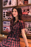 Woman in a red and black checkered dress standing in front of Japanese advertisements.