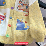 Yellow cardigan with cat-themed patches and buttons on a chair.