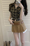 Person wearing a plaid shirt and brown skirt in front of a white door.
