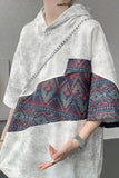 Person wearing a white hoodie with a patterned skirt against a gray background