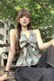 Woman wearing a plaid dress with a large bow sitting outdoors.