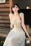 Woman in a polka dot dress sitting on a wooden bench outdoors.