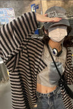 Person wearing a striped sweater, gray crop top, and cap with text in an indoor setting.