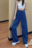 Person wearing blue pinstripe pants and a white top against a wooden wall.