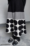 Person wearing a black and white polka dot skirt with a plain background