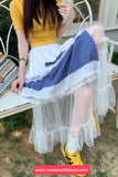 Person wearing a yellow top and white skirt with blue plaid pattern, sitting on a bench.
