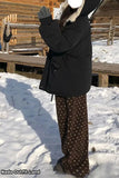 Person wearing a black coat and patterned pants standing in a snowy landscape with wooden structures.
