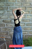 Person wearing a black top and blue jeans standing against a brick wall.