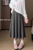 Person wearing a white sweater, gray pleated skirt, and pink shoes in a room.
