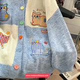 Children's cardigan with cat designs and colorful buttons on a chair.