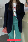 Person wearing a dark blazer, colorful shirt, and teal pants with a red and white striped bag.