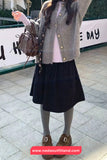 Person wearing a gray cardigan, black polka dot skirt, and brown shoes on a sidewalk.