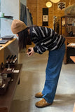 Person in a casual setting wearing a striped sweater and blue jeans.