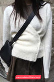 Person wearing a white sweater and brown skirt with a black crossbody bag against a stone wall.