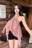 Woman in a red and white checkered dress with black shorts standing in front of a wooden wall.
