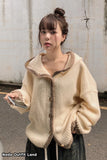 Woman wearing a beige knitted sweater with a hood against a plain background