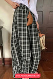 Person wearing plaid pants with a white shirt and brown bag in a room.