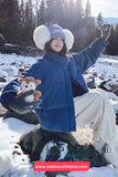 Person in winter clothing sitting on a rock in a snowy landscape with a teddy bear.